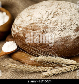 Traditionelle frisch gebackenes Brot auf einem Holzbrett, hölzerne Schüssel und Löffel mit Mehl. Alten Stil Stockfoto