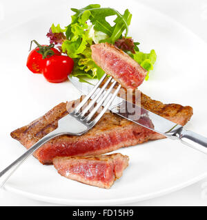 Gegrilltes Rindersteak mit Gemüse und Salat auf weißen Teller. Besteck - Messer und Gabel Stockfoto