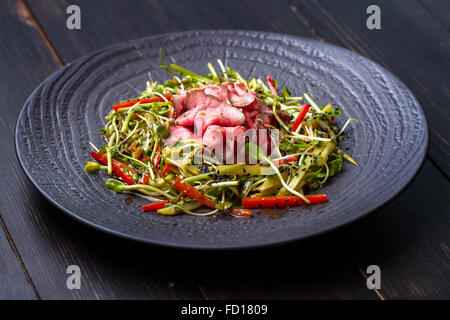 Authentische Salat mit Speck, frische rote Paprika, Sprossen, Sesam und Olivenöl auf einer schwarzen Platte. Morgen stimmungsvolle Beleuchtung, Stockfoto