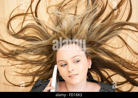 Kopf und Schultern, blonde Teenager Blue Eyed Girl Festlegung auf Holz, am Telefon sprechen. Haar verspritzt Wild hinter ihr. Stockfoto