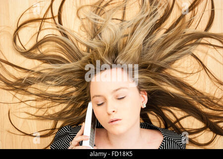 Kopf und Schultern, blonde Teenager Blue Eyed Girl Festlegung auf Holz, am Telefon sprechen. Haar verspritzt Wild hinter ihr. Stockfoto