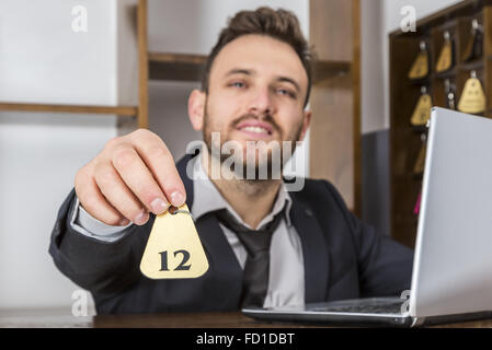 Bild der Empfangsdame an seinem Schreibtisch, geben den Schlüssel an einem Client. Selektiven Fokus auf dem Schlüssel. Stockfoto