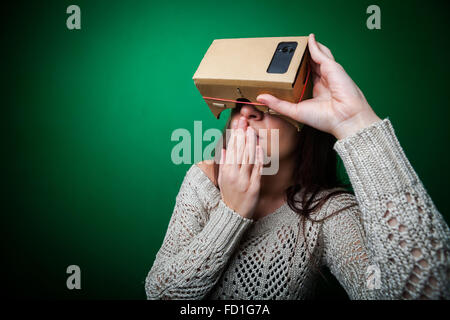 Farbe Schuss einer jungen Frau, die durch eine Pappe, ein Gerät, mit denen man virtuelle Realität auf ein mobile Phon erleben kann Stockfoto