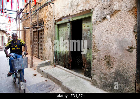 Stone Town (Sansibar), Tansania - 1. Januar 2016: Ein junger Mann mit dem Fahrrad vorbei an einer alten Mauer in Stonetown, Zanzibar. Stockfoto