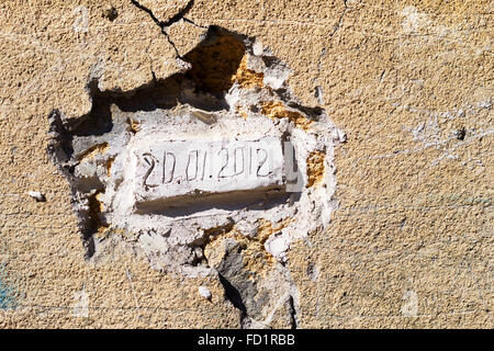 Backsteine gelegt in einer alten Mauer mit dem Datum des Lesezeichens. Schmutzige Betonwand mit Rissen und Kratzern. Dringende Reparaturen erfordert Stockfoto