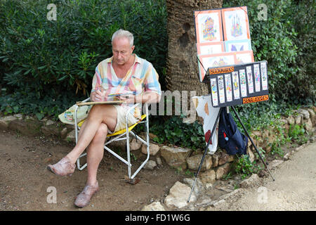 Verschiedene Standorte im Parc Güell, Barcelona. Englischen Exklaps Künstler Malerei während sitzt und seine Kunst zu verkaufen. Stockfoto