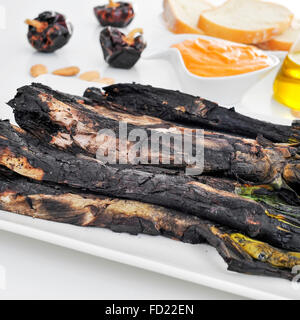 Nahaufnahme einer Platte mit einigen gegrillte Calcots, süße Zwiebeln und eine Schüssel mit Romesco-Sauce, typisch für Katalonien, Spanien, auf einem Satz Stockfoto