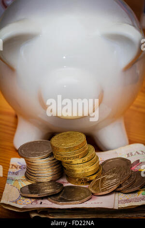 Weiß gefärbte Keramik Sparschwein mit Banknoten und Münzen GBP Stockfoto