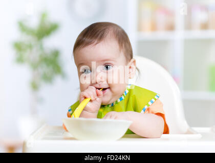 Baby Kind sitzt im Stuhl mit einem Löffel Stockfoto