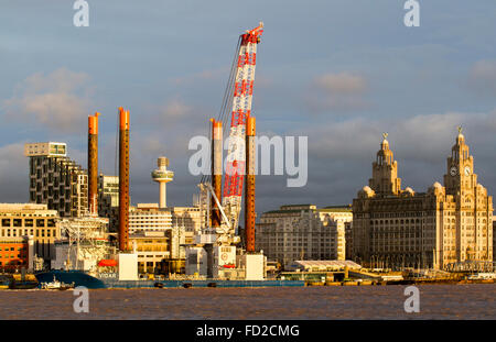 Die Offshore-Jack-up-Rig, Arbeitsbühne & Kranschiff Vidar, vertäut am Kreuzfahrtterminal, Hafen von Liverpool für Reparaturen. Im Besitz der in Luxemburg ansässigen Jan de Nul Group, die Dienstleistungen für maritime Infrastruktur bietet. Es hilft bei Bau und Wartung das Schiff ist 140,4m in der Länge. Der Schwerlastkran kann bis zu 1200 Tonnen heben und ist im Hafen, um mit Geräten speziell für die Installation von Offshore-Windparks ausgestattet werden. Die Skyline von Liverpool und die drei Wahrzeichen von Liverpool. Stockfoto