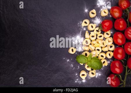 Tortellini, Tomaten, Basilikum und Mehl auf einem schwarzen Steinplatte. Draufsicht mit Exemplar Stockfoto