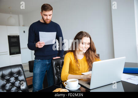 Porträt von ein glückliches junges Paar bezahlen ihre Rechnungen online mit Laptop zu Hause Stockfoto