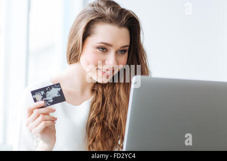 Lächelnde Frau mit Laptop-Computer und EC-Karte zu Hause halten Stockfoto
