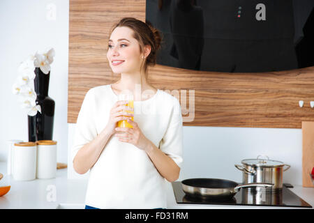 Glücklich attraktive junge Frau in der Küche stehen und Orangensaft trinken Stockfoto