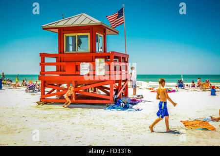 Kinder spielen am Strand an einem heißen sonnigen Tag unter die Sonnenanbeter in der Nähe von der berühmten roten Strandwache auf Siesta Beach, FL Stockfoto