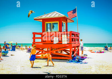 Kinder spielen am Strand an einem heißen sonnigen Tag unter die Sonnenanbeter in der Nähe von der berühmten roten Strandwache auf Siesta Beach, FL Stockfoto