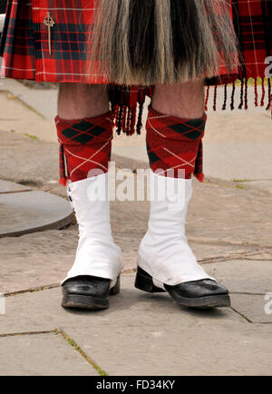 Beine und Schuhe von einem ständigen schottischen Mann gekleidet in einen roten aufgegebenes Tartan Kilt. Stockfoto