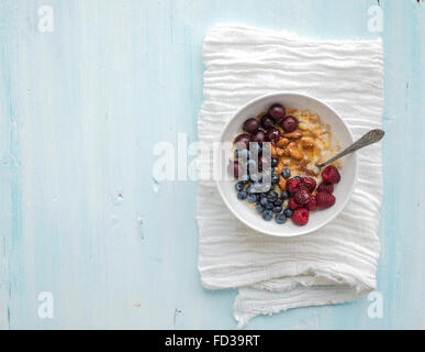 Gesunden Frühstücks-Set. Schüssel mit Hafer Porridge mit frischen Beeren, Mandeln und Honig über weiße Serviette. Ansicht von oben Licht blau backdro Stockfoto