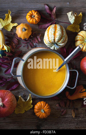 Kürbis und Süßkartoffeln Suppe in einen Kochtopf, Herbst Blätter und verschiedene Kürbisse Sorten auf einem rustikalen Holztisch Stockfoto