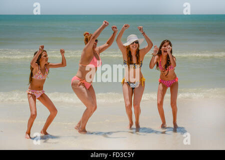 Vier jubelnde Frauen in Bikinis zu feiern, lachen und Ausgelassenheit in der Brandung am Strand Stockfoto