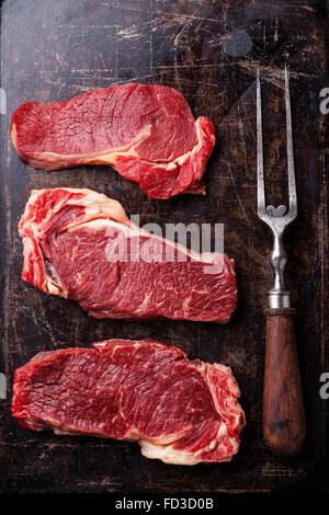 Rohes Frischfleisch Ribeye Steak und Fleischgabel auf dunklem Hintergrund Stockfoto