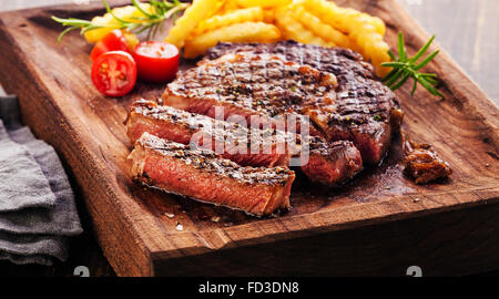 In Scheiben Ribeye Steak mit Pommes Frites auf dem Board Block auf hölzernen Hintergrund Stockfoto