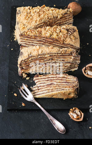 In Scheiben geschnitten hausgemachte Honigkuchen mit Schokolade Creme und Walnüsse, serviert mit Dessertgabel und gehackten Nüssen auf Schiefer Tafel. Nach oben Stockfoto