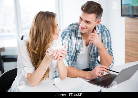Lächelnde Kollegen in Freizeitkleidung arbeiten mit Laptop und Kaffee trinken Stockfoto