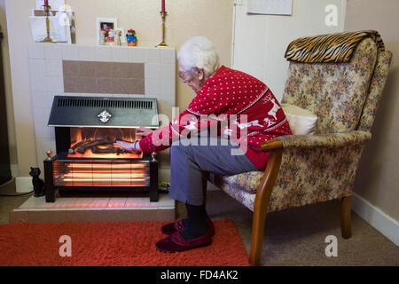 Rentner neben elektrischen Feuer warm zu halten Stockfoto