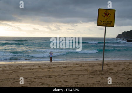 Eine gefährliche Brandung, ein Warnschild und eine Person, die die Wellen und das Meer am Bondi Beach in Sydney, Australien, beobachtet Stockfoto