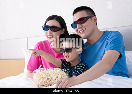 Familie vor dem 3D Fernseher im Bett mit popcorn Stockfoto