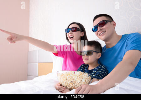 Familie vor dem 3D Fernseher im Bett mit popcorn Stockfoto