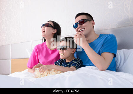 Familie vor dem 3D Fernseher im Bett mit popcorn Stockfoto