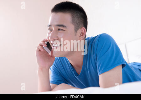 Junger Mann mit Smartphone im Bett Stockfoto