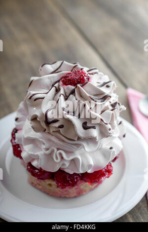 Einzelne Vanille Cupcake mit Frischkäse Zuckerguss verziert mit roten Johannisbeeren und Schokolade auf dem hölzernen Hintergrund Stockfoto