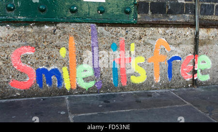 „Smile its free“ auf einer Wand in der Brick Lane gemalt, Glückskonzept. Farben und Formen. Positive Zufriedenheit. Achtsamkeit. Graffiti London. Stockfoto