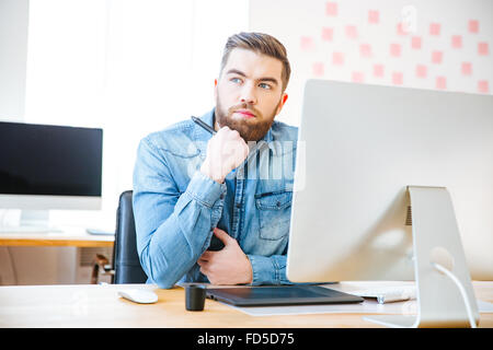 Nachdenklich attraktive moderne Designer sitzen am Arbeitsplatz im Büro und denken Stockfoto