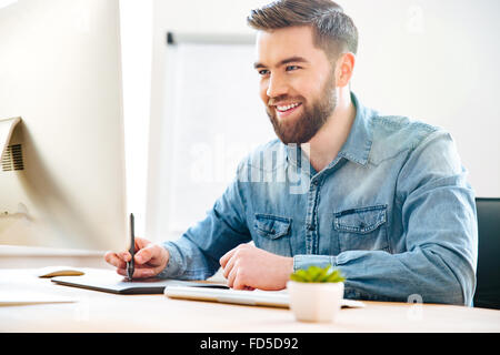 Glücklich attraktive junge männliche Designer im Büro sitzen und zeichnen auf Grafiktablett Stockfoto