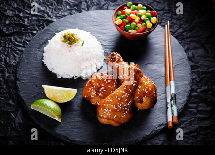 Gebratene Hähnchenschenkel mit Teriyaki sauce, Sesam und Reis auf schwarzem Stein Stockfoto