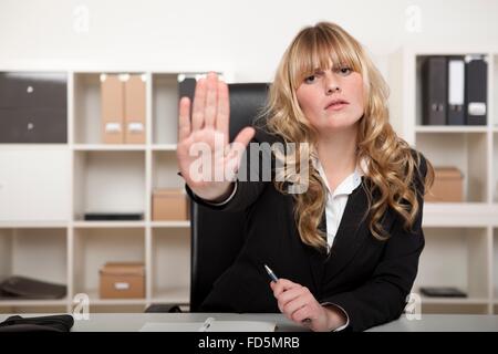 Junge Geschäftsfrau stoppen hielt ihre Hand in der Luft mit einem strengen Ausdruck, als sie hinter ihrem Schreibtisch sitzt Stockfoto