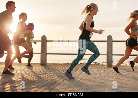 Porträt des jungen Menschen direkt an Strandpromenade laufen. Männer und Frauen laufen Marathon unterwegs am Meer bei Sonnenuntergang. Stockfoto