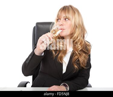 Junge Geschäftsfrau nippen Champagner aus einem eleganten Querflöte an ihrem Schreibtisch, als sie einen geschäftlichen Erfolg oder Sieg feiert Stockfoto