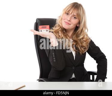 Erfolgreiche junge Geschäftsfrau mit einem Musterhaus ausgeglichen auf ihrem Palm mit einem stolzen Lächeln in die Kamera schaut Stockfoto