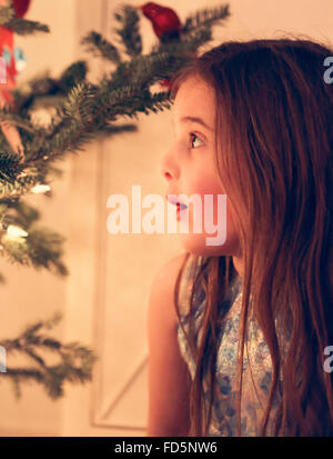 Profil von einem kleinen Mädchen starrte auf einen leuchtenden Weihnachtsbaum mit einem Blick der Wunder auf ihrem Gesicht. Stockfoto