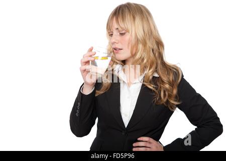 Junge berufstätige Frau in einem smart schwarz Jacke steht ihr Durst trinken ein Glas reines gesundes Wasser und Zitrone Stockfoto