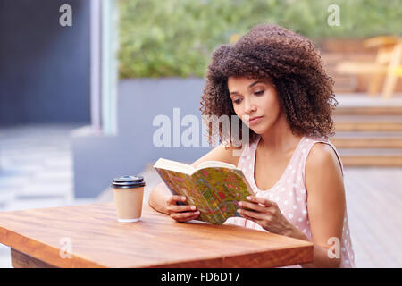 Schöne Frau, die ein Buch draußen mit Kaffee zum mitnehmen Stockfoto