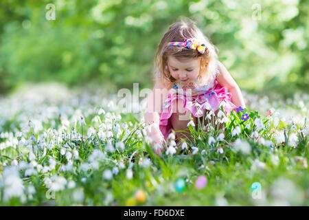 Kleines Mädchen Spaß auf Ostereiersuche. Kinder in blühenden Frühling Garten mit Blumen Krokus und Schneeglöckchen. Stockfoto