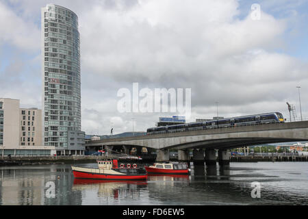 Blick über den Fluss Lagan Belfast in Richtung Obel-Apartmentgebäude Belfast mit NIR-Zug, der den Fluss Lagan auf der Traverse mit dem Hafen überquert. Stockfoto