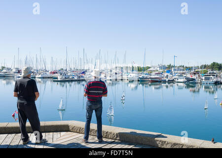 Gruppe von älteren Männern racing mit remote gesteuerten kleine Segelboote an einem hellen Sommertag in einer Marina. Stockfoto