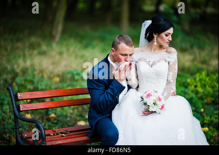 Junge stilvolle Hochzeitspaar auf Bank im Park sitzen Stockfoto